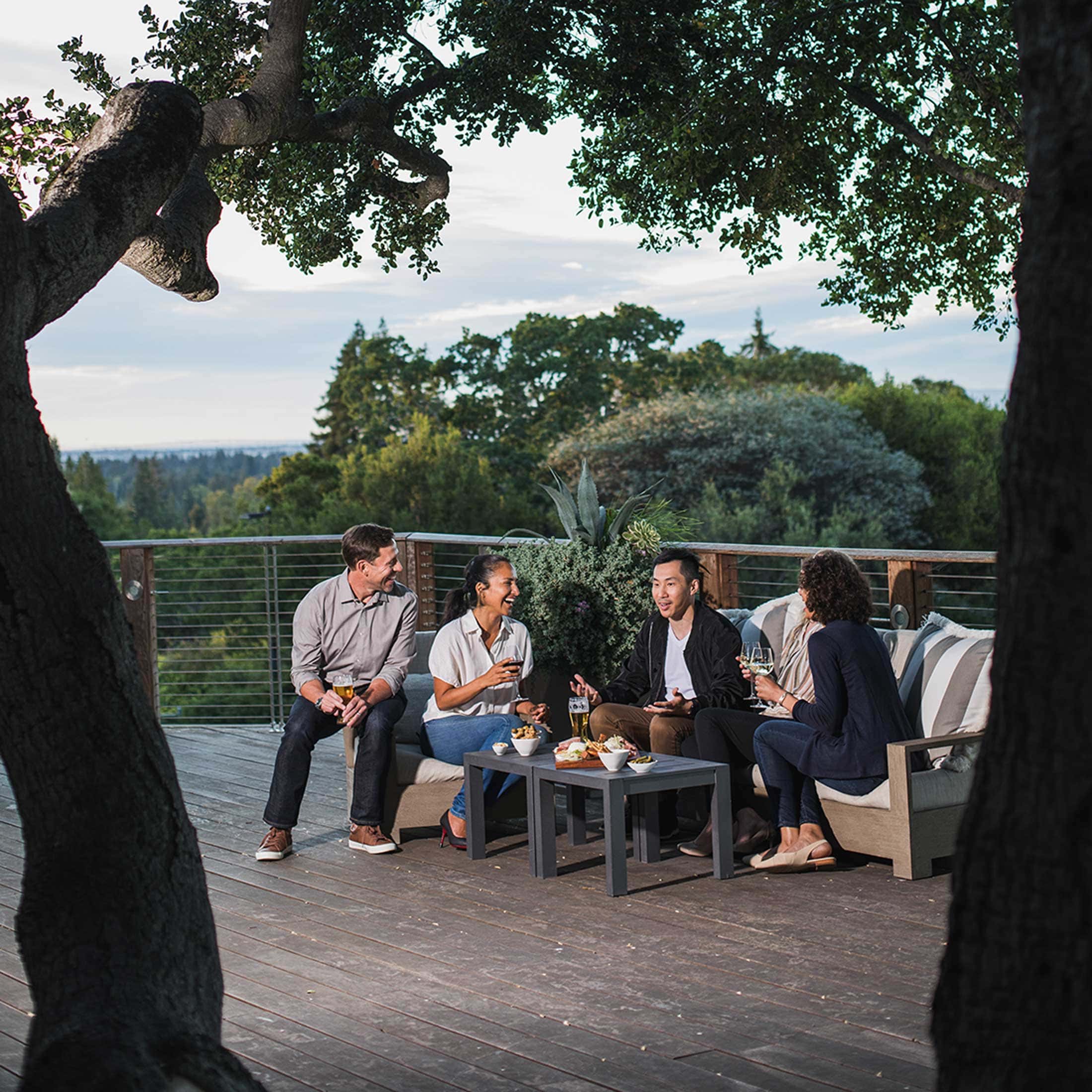 4 friends share drinks and food on a deck at sunset