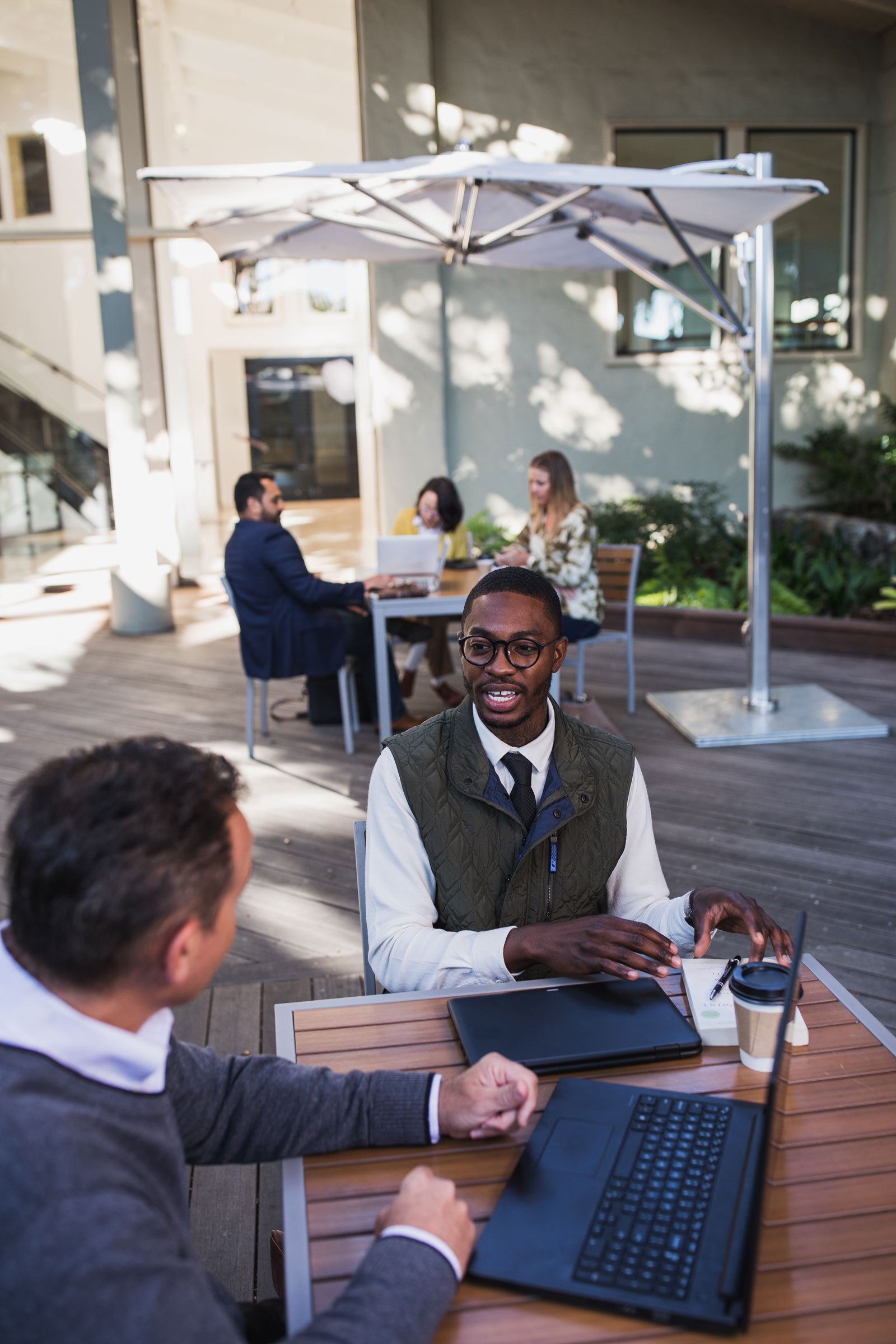 Two businessmen work outside together with laptops and coffee
