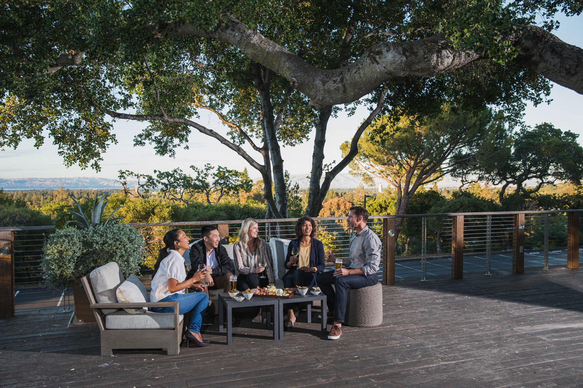A group of friends hang out at an outdoor sitting area with food and drinks