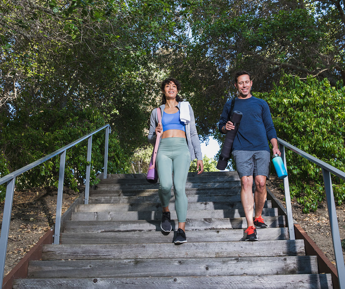 A man and woman carrying yoga mats walk down outdoor stairs