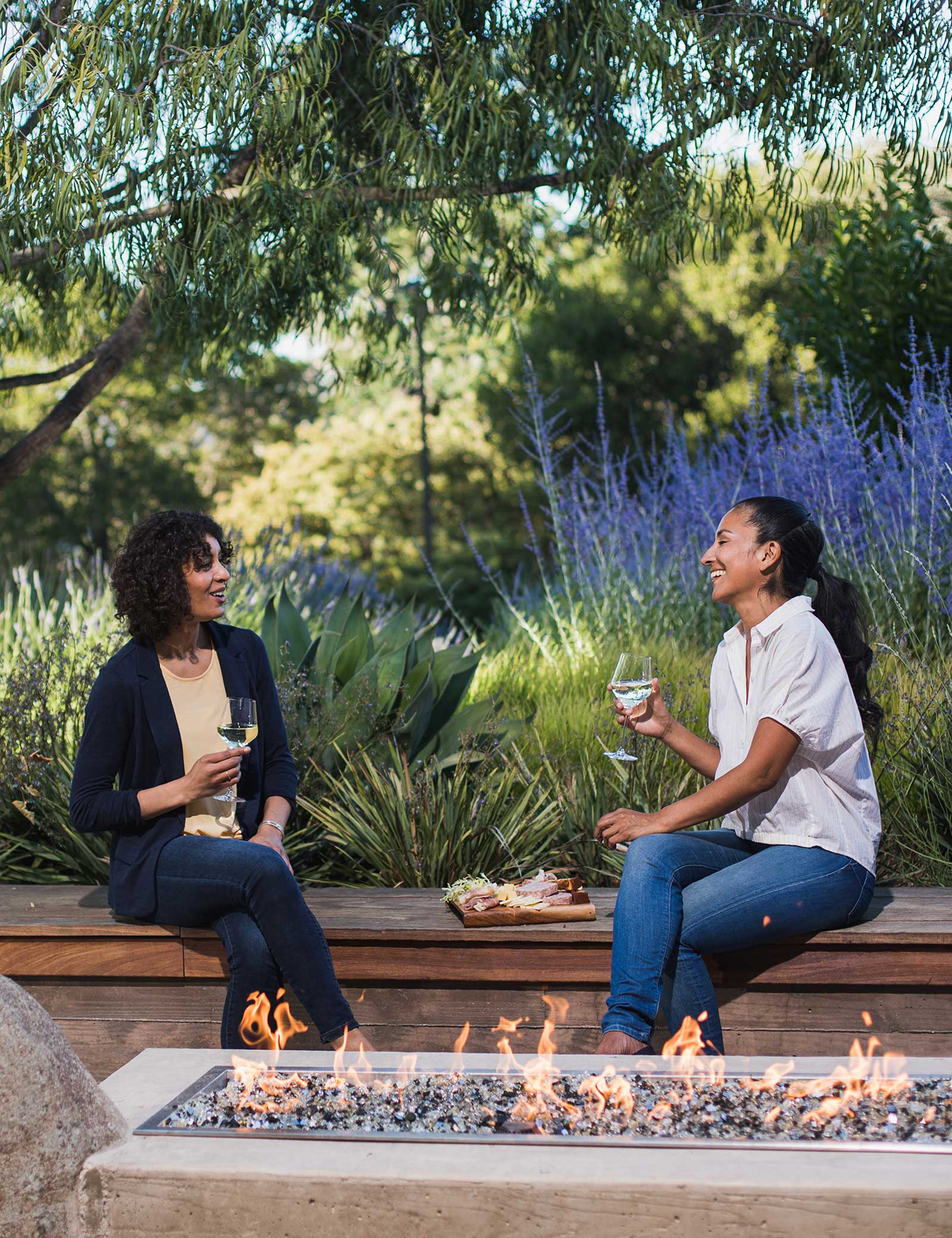 Two women share glasses of wine together on a courtyard bench