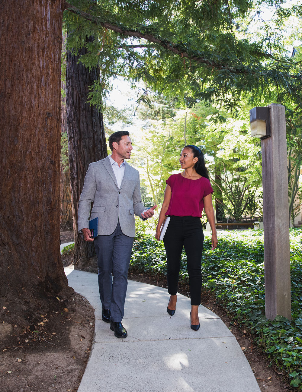 A man and woman walk together down a sidewalk surrounded by greenery