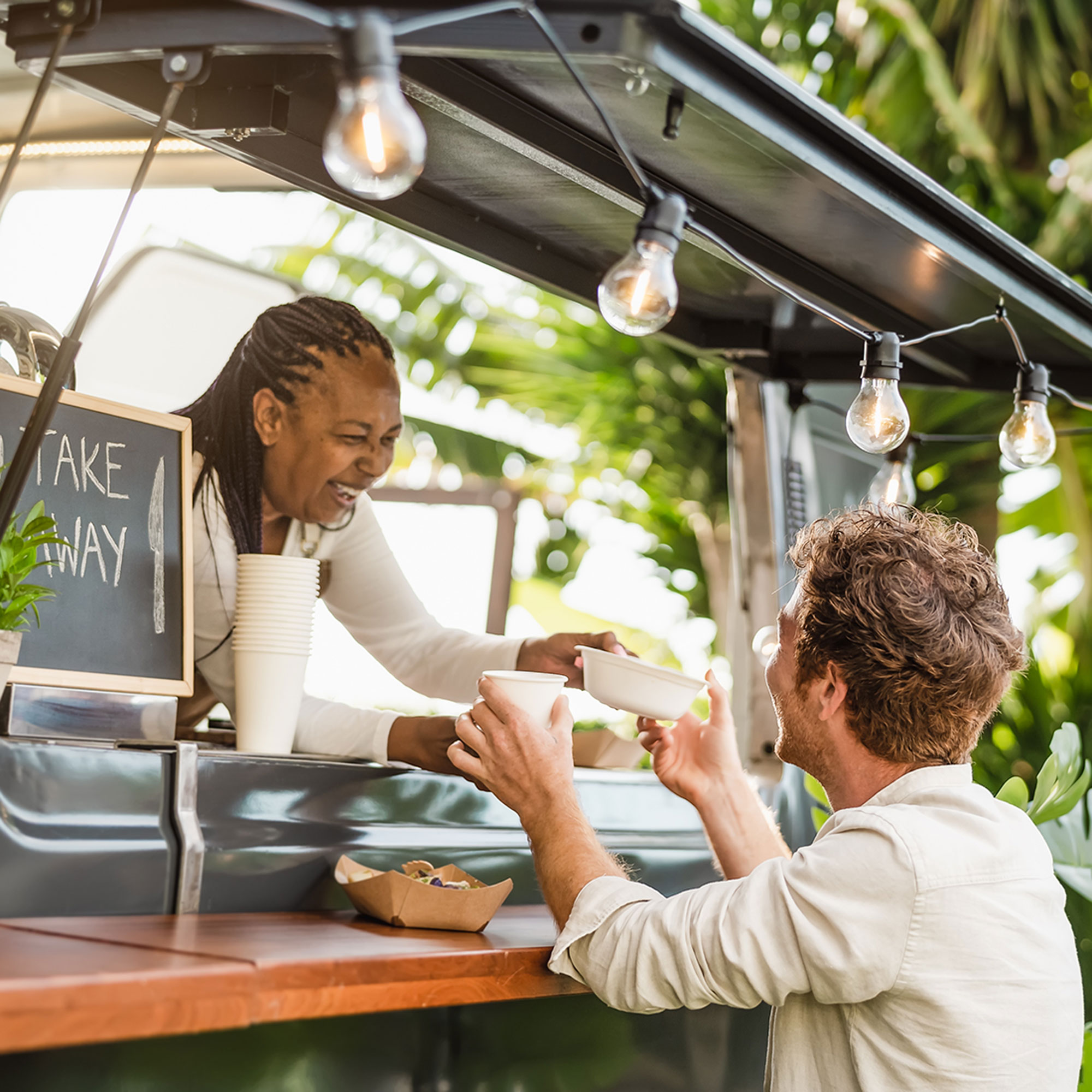 A woman hands a man a plate and drink from a food truck
